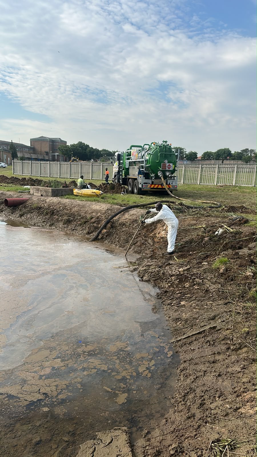 Crew desilting a pollution control dam with a suction hose and vacuum tanker